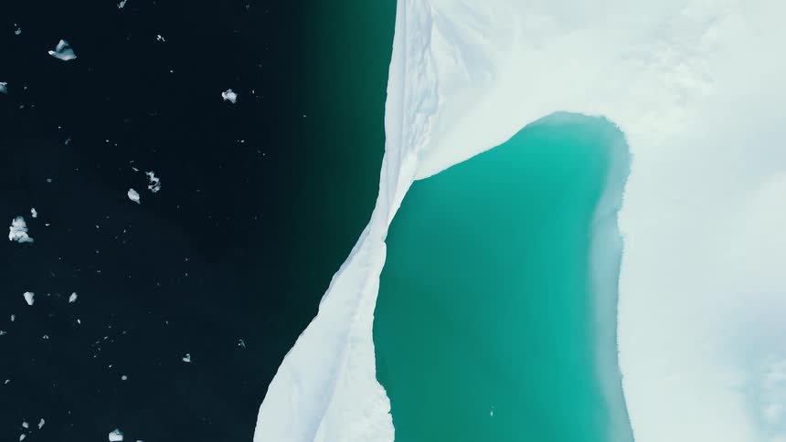 An abstract overhead aerial view shows the stark contrast between the bright white fractured ice of a glacier and the deep black and vibrant turquoise water of the cold sea