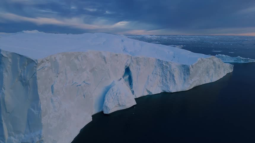 A flat slab of sculpted ice lies on a frozen expanse as sunlight filters through layered clouds
