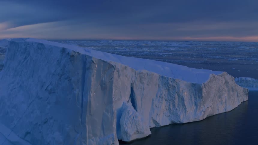 Aerial view of a massive iceberg floating in the arctic ocean at dusk