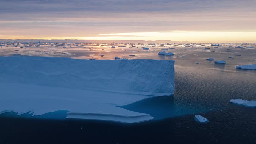 A vast field of fragmented ice spans calm water beneath a blue sky