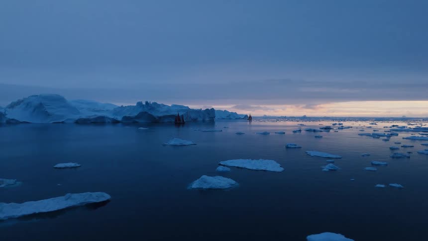 A blue sea dotted with ice floes stretches toward a pale band of light on the horizon