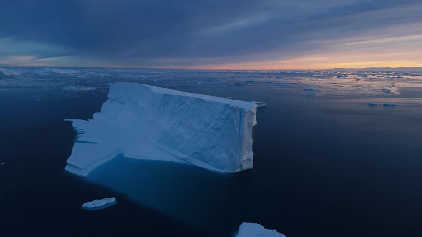 Massive flat topped iceberg in dark ocean under a twilight sky