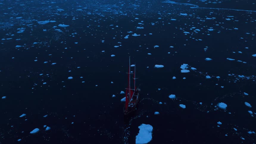 Aerial view of sailboat gliding through icy ocean at twilight