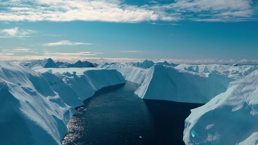 Massive icebergs frame a dark water channel under a bright sky