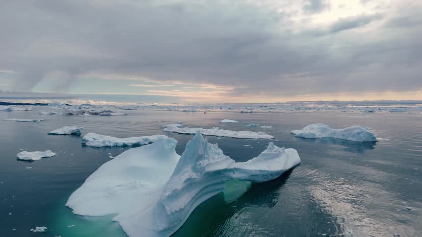 Aerial view of icebergs floating in a vast ocean under a cloudy sky