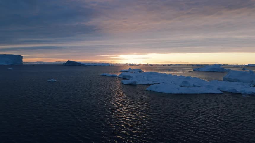 Aerial view of icebergs floating in dark ocean water at sunset under a cloudy sky