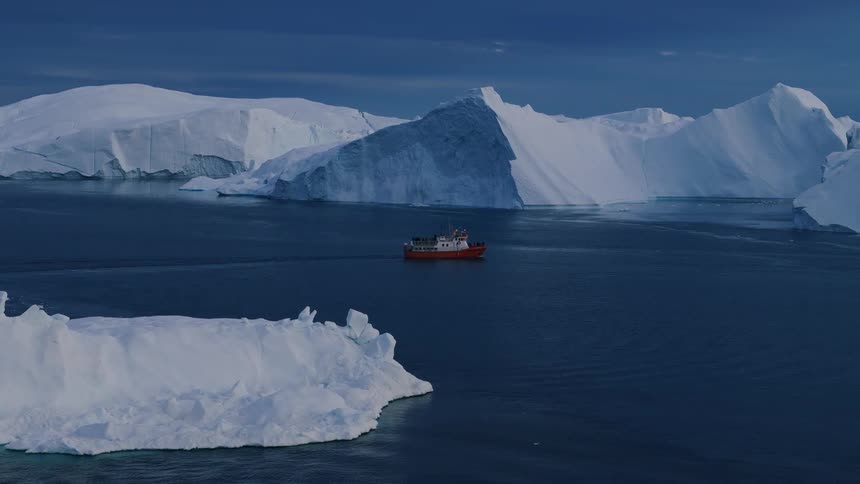 Aerial view of a small red boat navigating among icebergs in dark blue water
