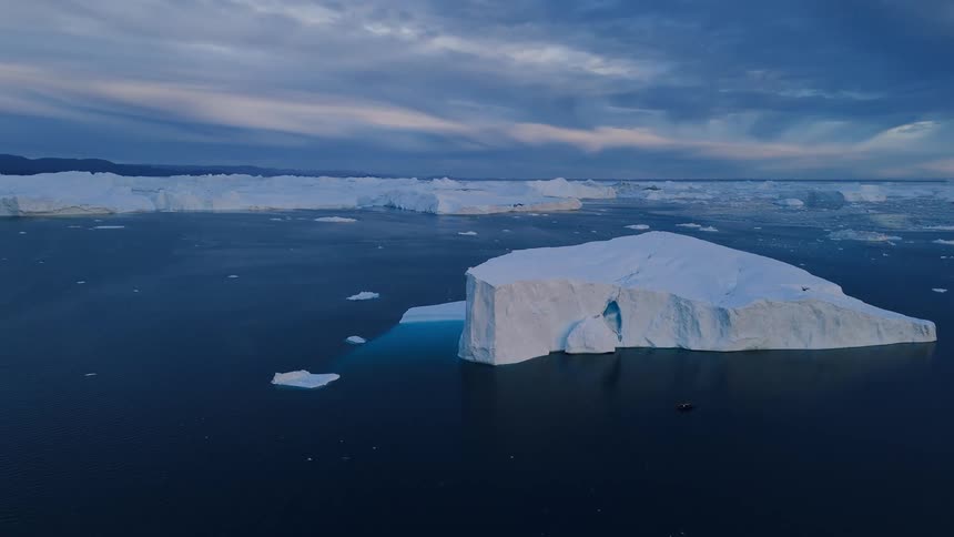 Aerial view of a massive iceberg with an arch in the dark ocean at twilight