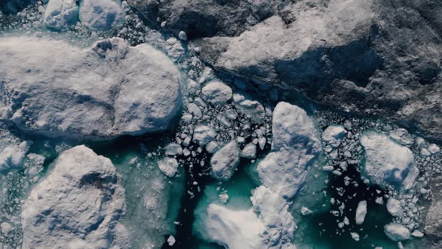An overhead aerial shot captures a dense mosaic of white ice floes and broken chunks of ice floating in a black and deep turquoiseblue water channel the scene highlights the contrast between the massive pieces of ancient fractured white ice and t