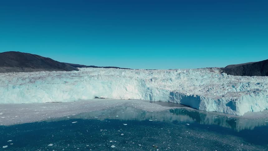 A wide glacier front lines a calm icy bay under a deep blue sky