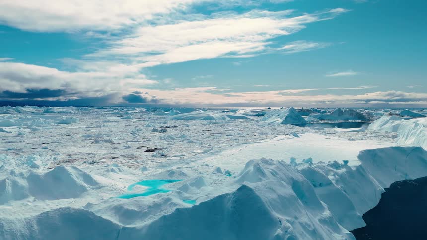 A wide expanse of broken white ice covers a large area deep blue water channels and ponds wind through the formation large chunks of ice create steep walls all under a blue sky with white clouds