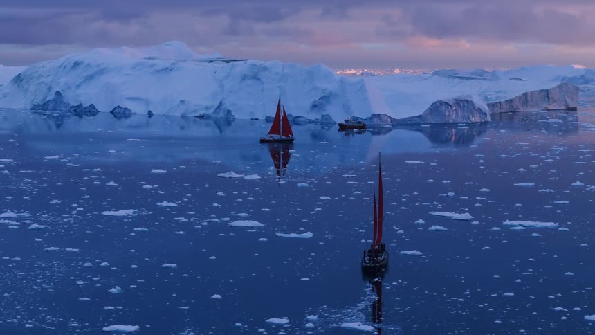 Aerial view of two red sailed sailboats in arctic waters near glaciers at sunset