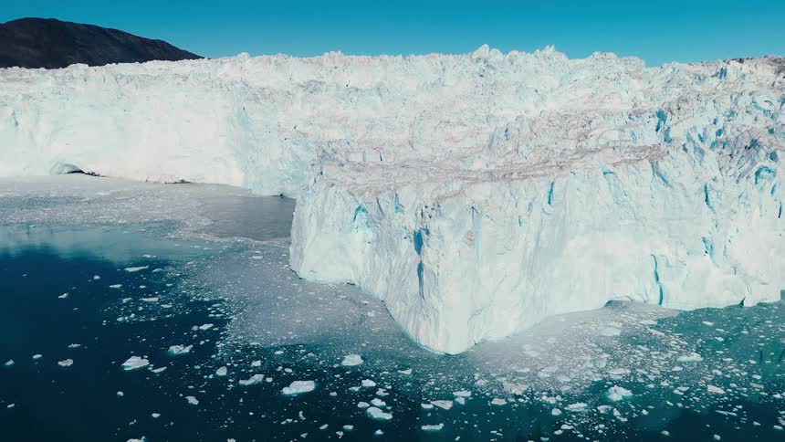 The immense textured white wall of the glacier slowly recedes revealing the sheer scale of the cliff as it meets the deep blue icescattered arctic water below