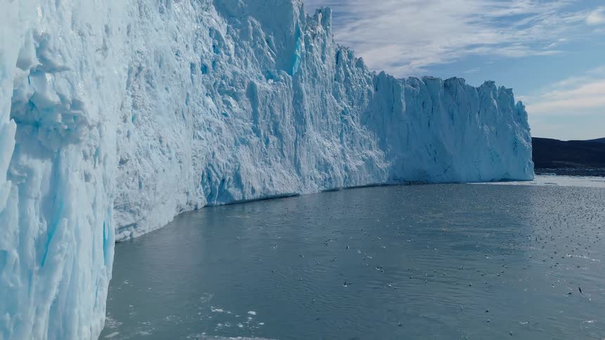 A towering blue iceberg looms above dark water in cool light