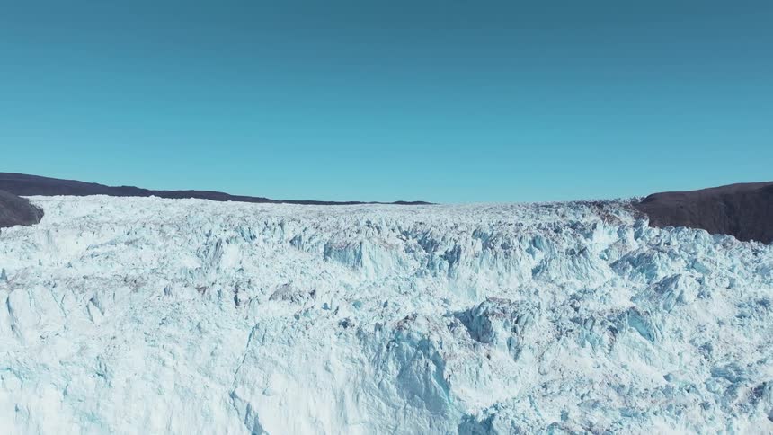 A vast jagged glacier stretches to the horizon beneath a cloudless blue sky