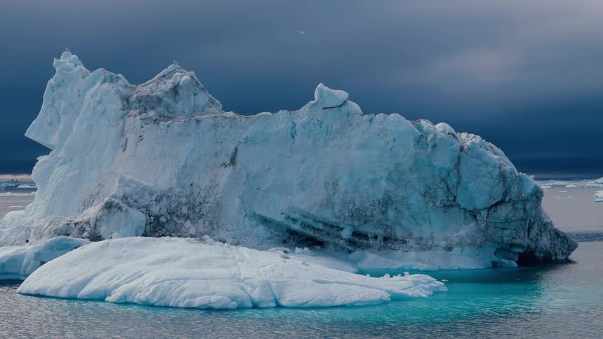 A jagged iceberg rises from teal water under a dark stormy sky