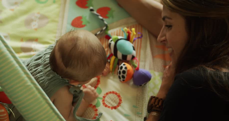A smiling mother watching her baby play with stuffed toys