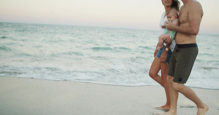 A young family of three walking across the seashore during daytime