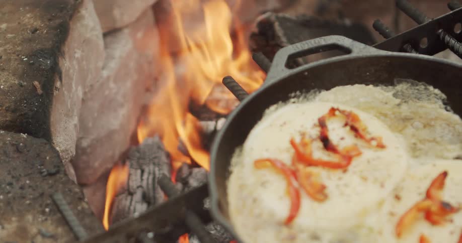 Cooking breakfast in a cast iron skillet outdoors on a camp fire