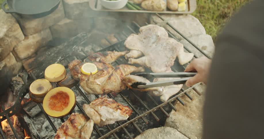 Person grilling chicken and vegetables over a campfire outdoors
