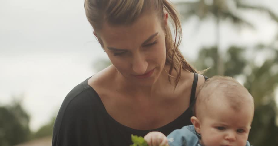 The woman holds her baby and eats a leaf
