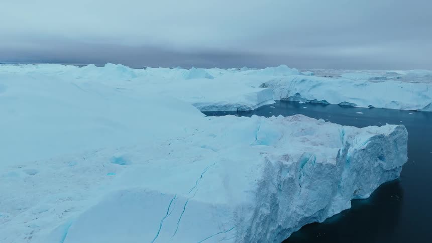 Cracked glaciers on the arctic coast with melting ice floating on the water