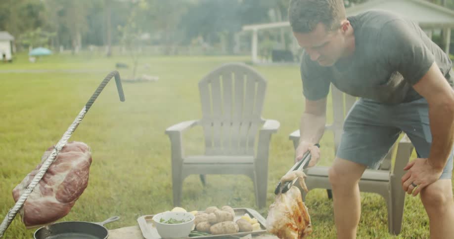 Man grilling poultry and vegetables over an outdoor fire pit