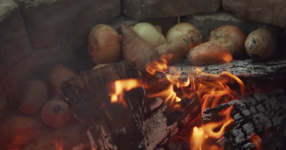 Closeup of potatoes baking over a campfire with glowing logs in the background