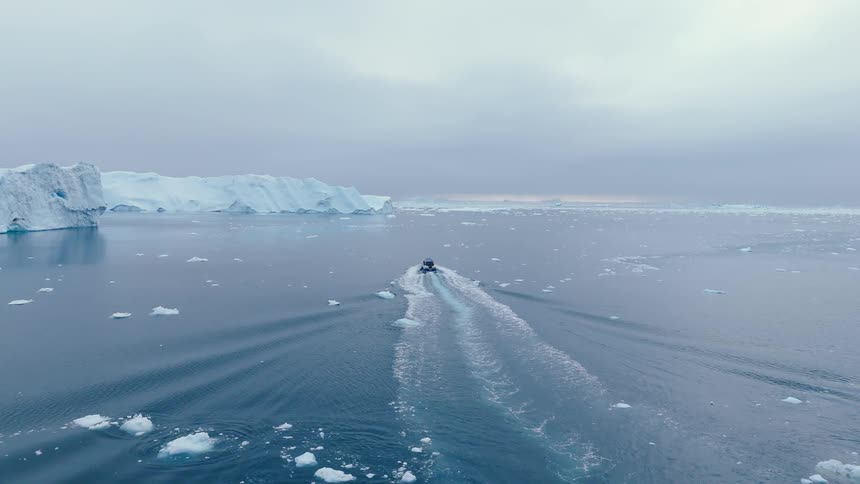 A small motorboat speeds through icy waters past large ice formations
