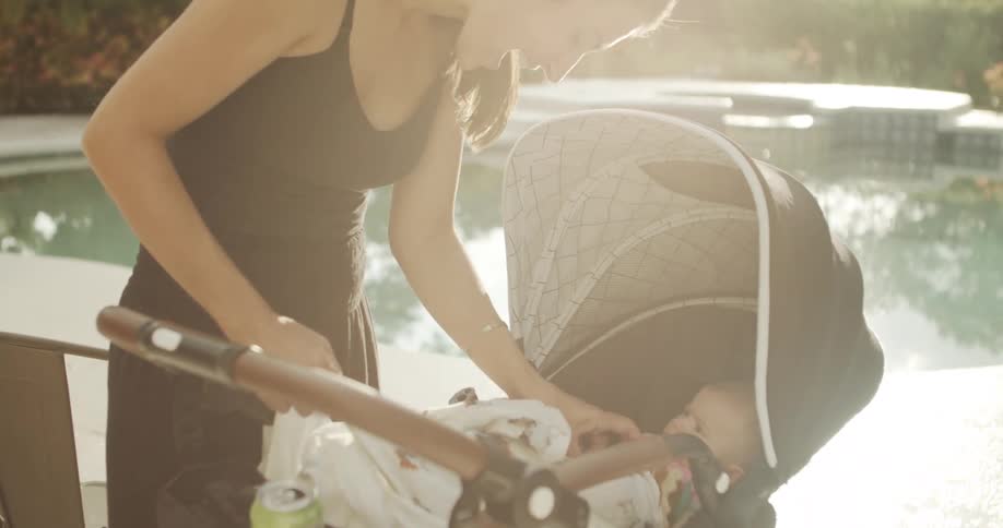 Mother playing with her baby in a stroller beside a pool outdoors