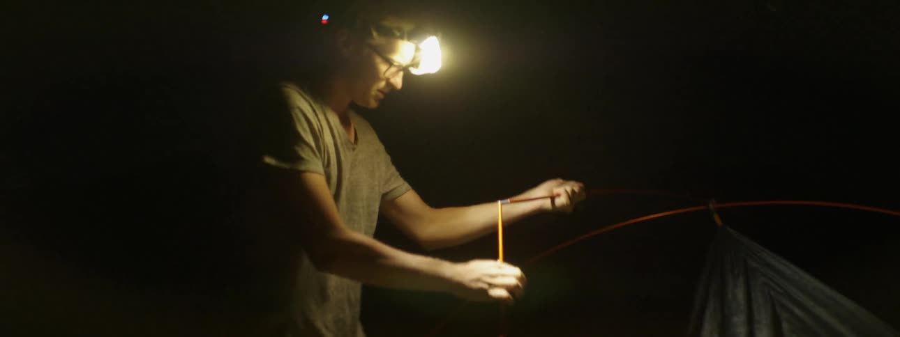 A man is putting together a tent at night time