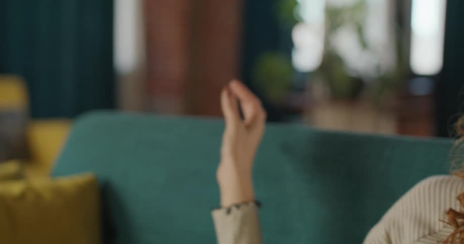 The video is a closeup shot of a pair of hands interacting with an invisible virtual interface performing gestures in the air the hands are slightly out of focus with a teal sofa visible in the blurred background suggesting a person is sitting