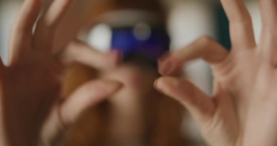 A woman with curly red hair wearing a vr headset smiles and makes framing gestures with her hands as the focus shifts in and out