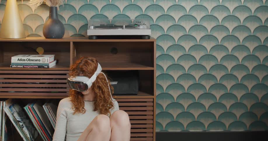 A young woman sitting leaning against a dresser wearing a virtual reality headset