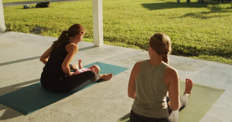 A woman is sitting on a yoga mat with her baby