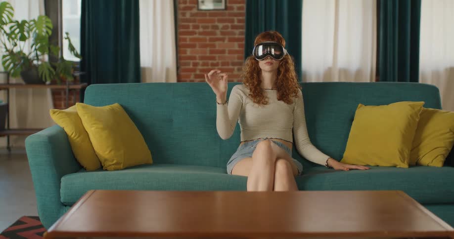 Teenage girl sits on the couch wearing a virtual reality headset moving her hands