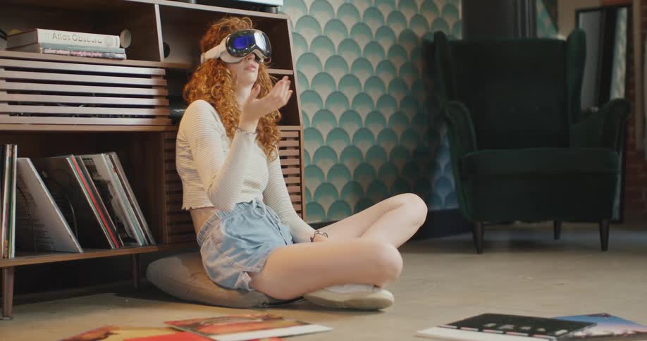 Teenage girl sitting on the floor wearing a virtual reality headset as she moves her arms