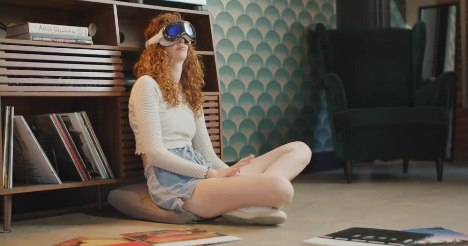 Teenage girl sitting on the floor wearing a virtual reality headset as she looks around smiling and laughing