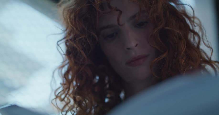 Redheaded woman reads while near the window