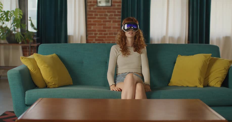 A female teenager using vr goggles while sitting on a couch in a living room during daytime