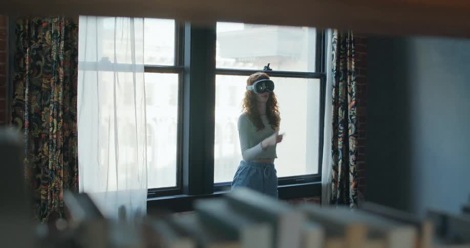 Teenage girl standing near a window wearing a virtual reality headset moving her hands