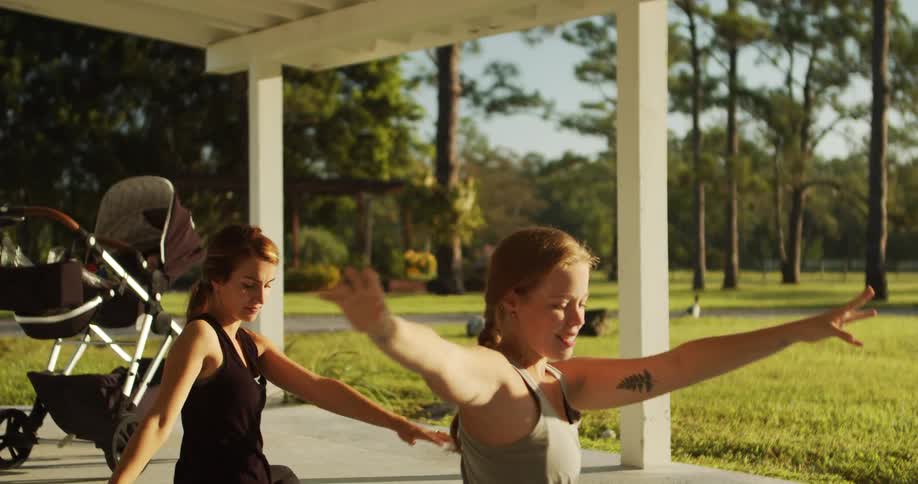 Two women practice yoga on a porch next to a stroller outdoors