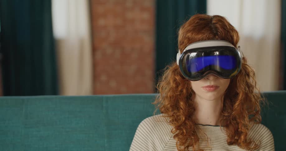 Teenage girl sitting on the couch wearing a virtual reality headset as she moves her hands