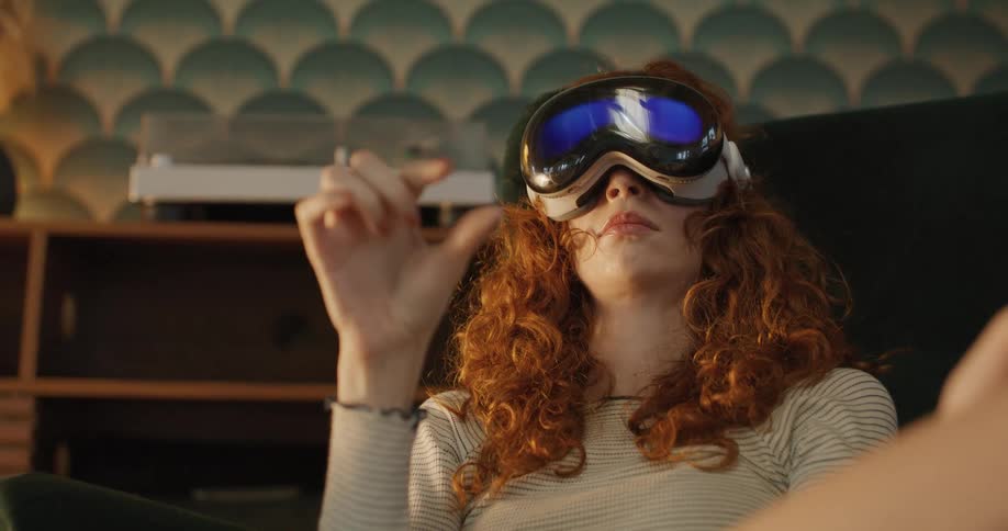 A woman with curly red hair gestures while using a virtual reality headset