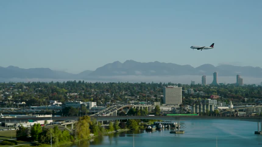 Airplane flying above a city skyline with distant mountains