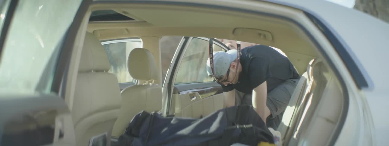 A man leans through an open car door to tie his shoe