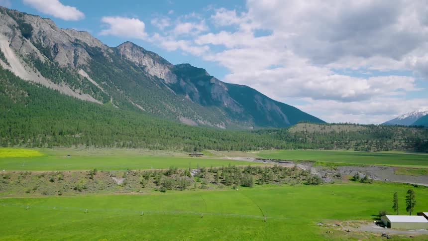 Aerial view of green fields with mountains under a partly cloudy sky