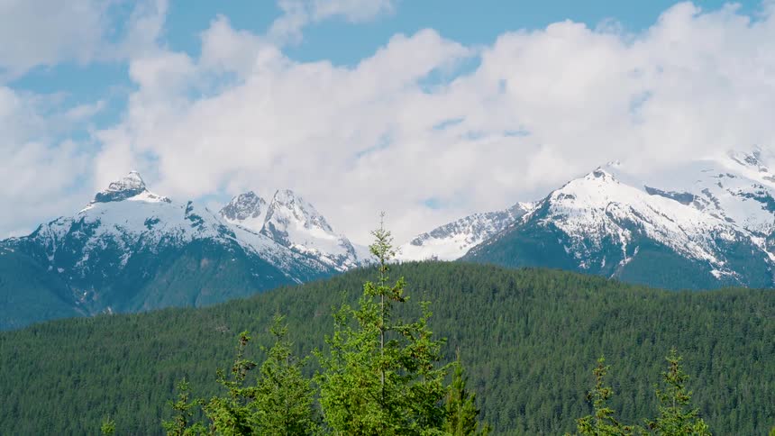 Aerial view moving over a forested mountain with snow covered mountains in the distance