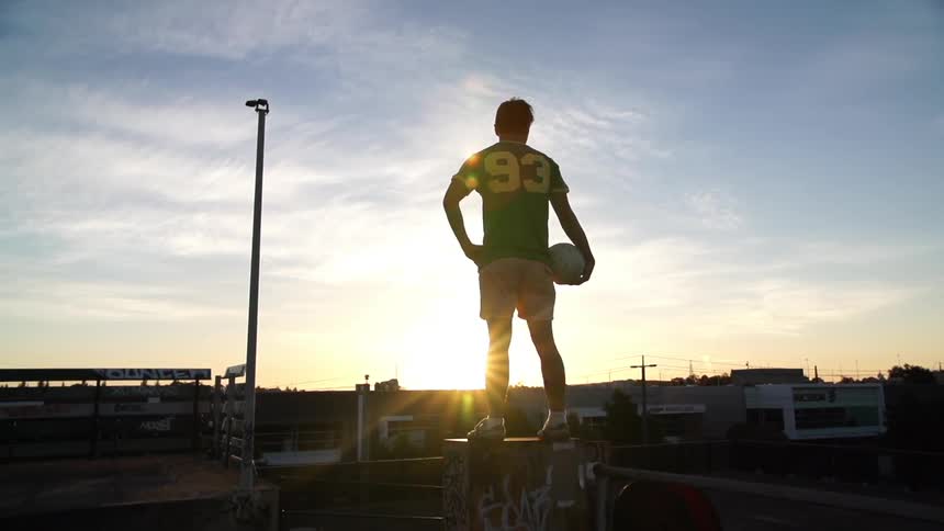 A man holding a soccer ball stands on a perch