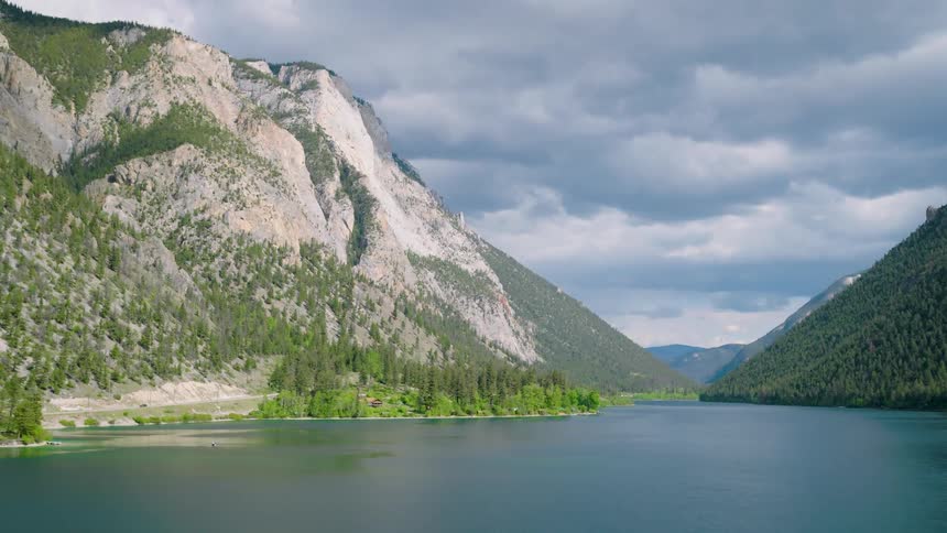 Calm blue lake surrounded by forested mountains under cloudy sky